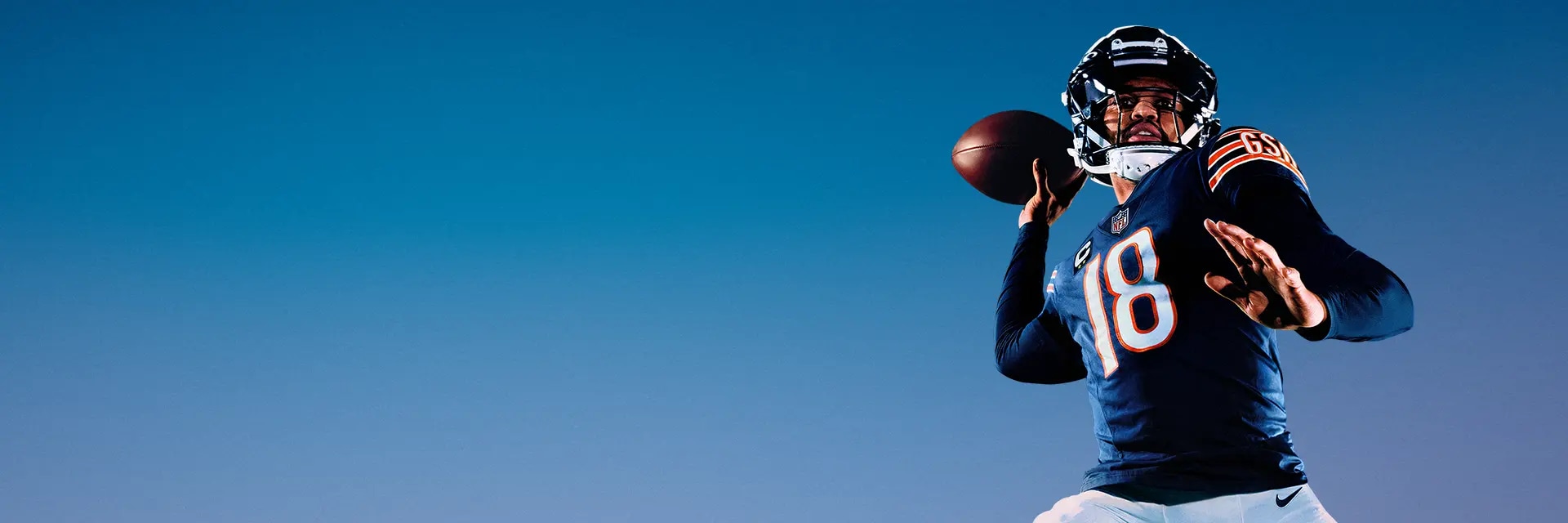 A quarterback poses mid-throw against a blue sky.