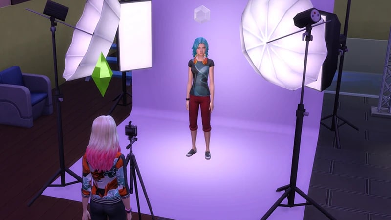 A Sim with blue hair stands in a photo studio while another Sim stands behind a camera, preparing to take a picture.