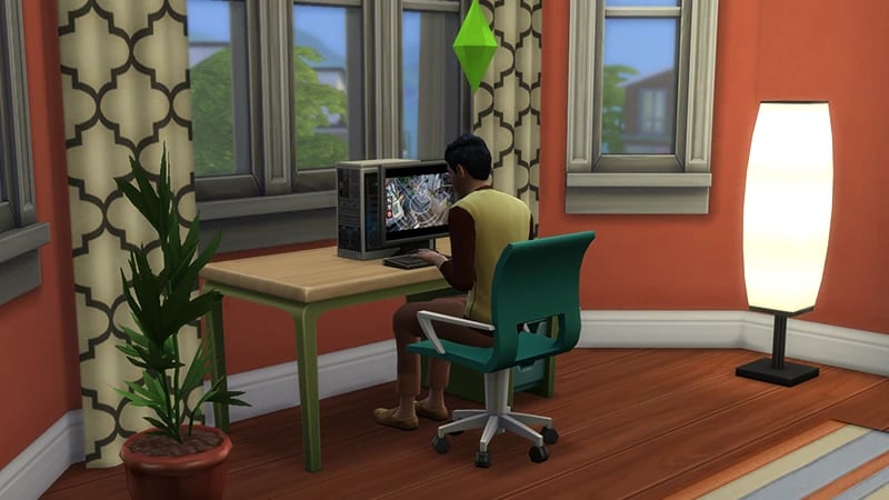 A Sim sits on a wheelie chair at a desk in front of a window, playing video games on a PC.