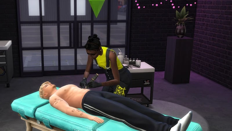 A topless Sim lies on a table while a Sim in a neon yellow top and black overalls tattoos his arm.