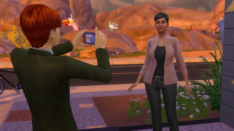 A red-haired Sim is snapping a photograph of another Sim with black hair wearing a pink blazer and black trousers.