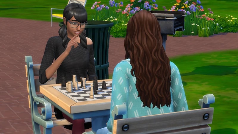 Cassandra Goth, wearing a black sweater and glasses, plays chess at a chess table in Magnolia Park in The Sims 4.