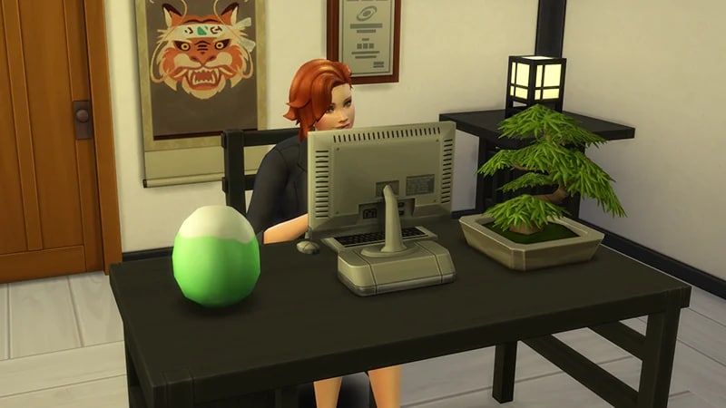 A red-haired Sim sits at a desk using the computer. On the desk is a plant and a Yamachan Simmi capsule.