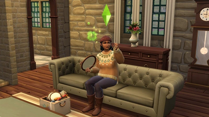 Sim vestindo um macacão estampado e um gorro vinho em um sofá, fazendo ponto-cruz com um aro de madeira.